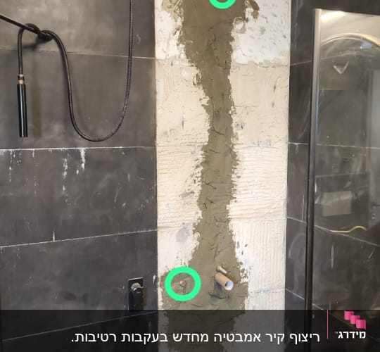 קיר אמבטיה בשיפוץ עם אריחים שחורים וצנרת חשופה